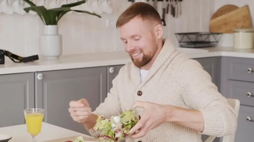 Homem sorrindo enquanto come uma salada